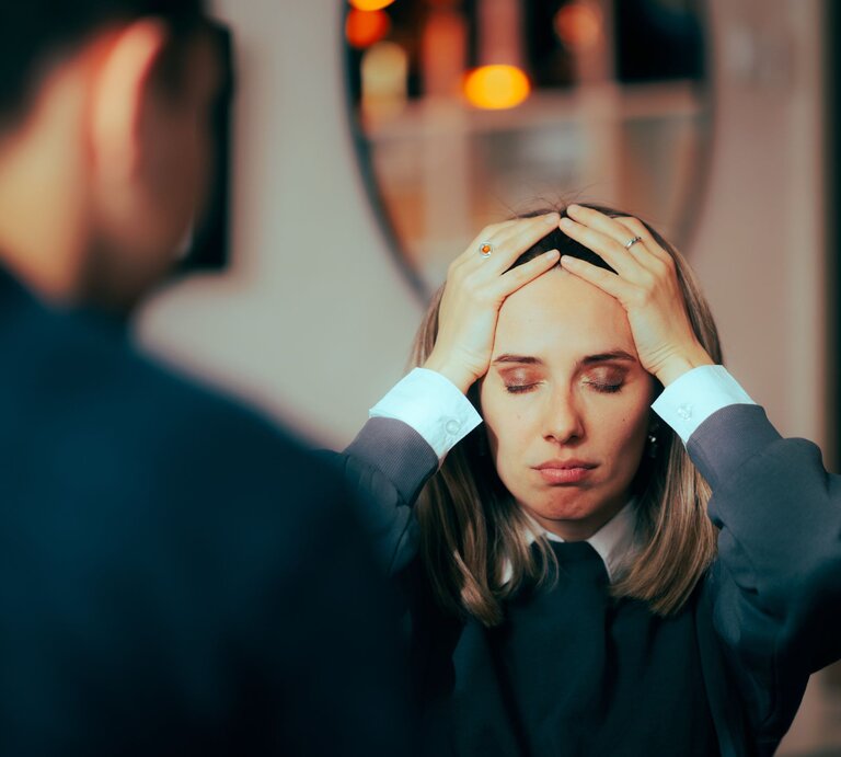 Frau und Mann in einer ernsten oder stressvollen Unterhaltung. Die Frau hält sich mit beiden Händen an den Kopf, die Augen geschlossen und einen besorgten Ausdruck im Gesicht. Der Mann, nur von hinten zu sehen, steht ihr gegenüber. | © Adobe Stock / nicoletaionescu