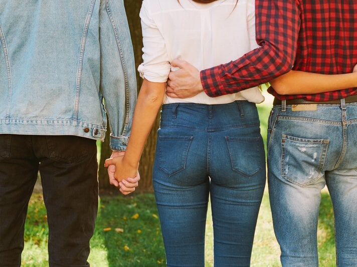 Drei Personen von hinten, die eng nebeneinander in einem Park stehen. Die mittlere Person, eine Frau, hält gleichzeitig die Hände von zwei anderen Personen an ihrer Seite. | © Shutterstock / golubovystock