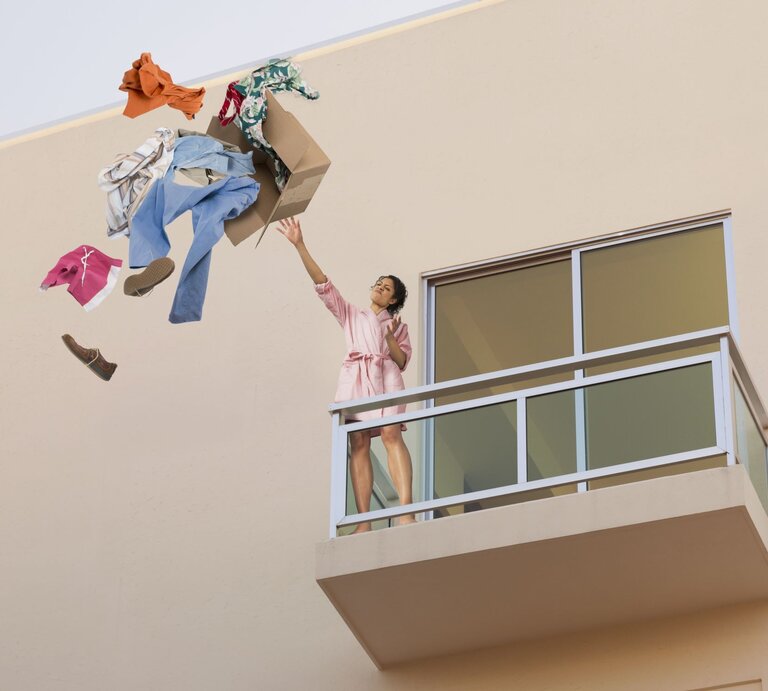 Eine Frau wirft einen Karton mit den Habseligkeiten ihres Ex-Freundes vom Balkon. | © gettyimages/John M Lund Photography Inc