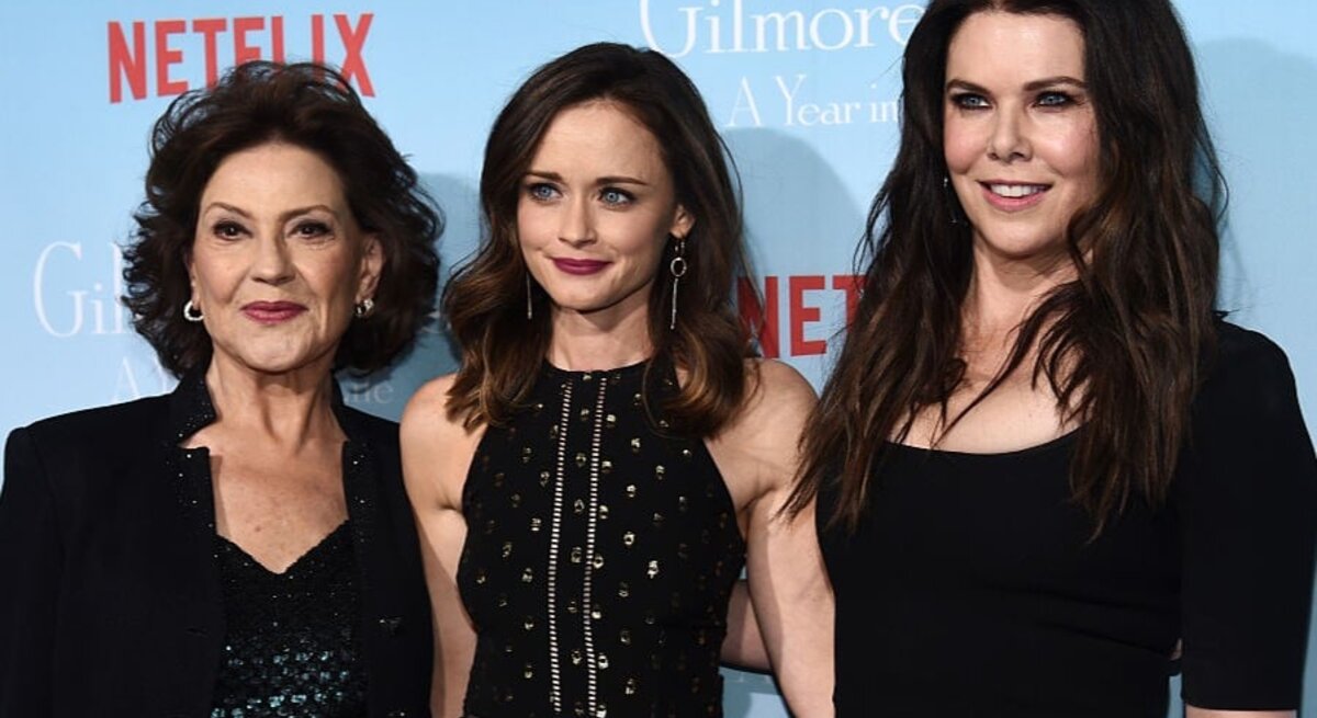 Drei Frauen stehen vor einer blauen Wand mit Netflix-Logo, stilvoll gekleidet in Schwarz, lächelnd und eng nebeneinander.