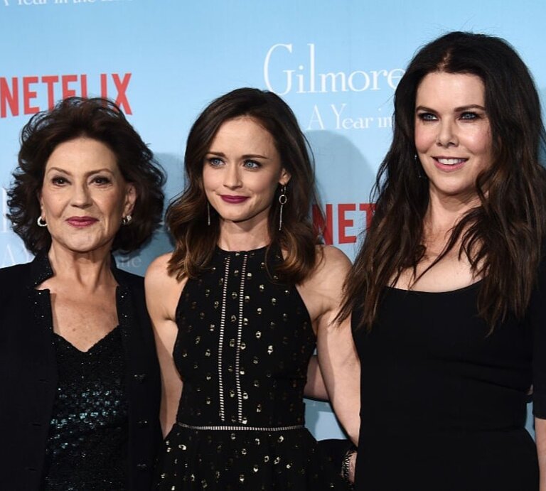 Drei Frauen stehen vor einer blauen Wand mit Netflix-Logo, stilvoll gekleidet in Schwarz, lächelnd und eng nebeneinander. | © Getty Images / Amanda Edwards 