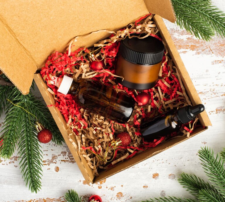 Kosmetik-Set in brauner Box mit rotem Füllmaterial, dekoriert mit Tannengrün und festlichen Christbaumkugeln. | © Shutterstock/Dasha_Romanova