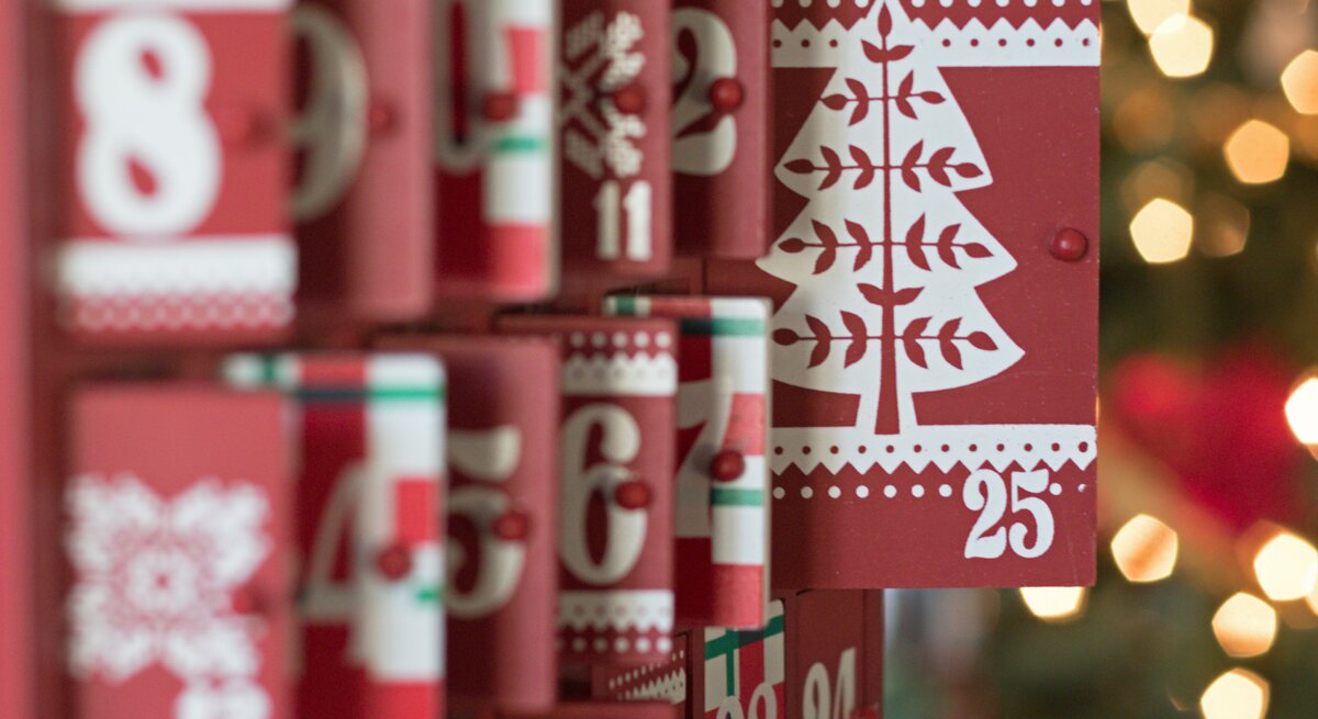 Roter Adventskalender mit weißen Zahlen und Weihnachtsbaum-Motiv auf Tür 25, weitere Türen teilweise geöffnet.