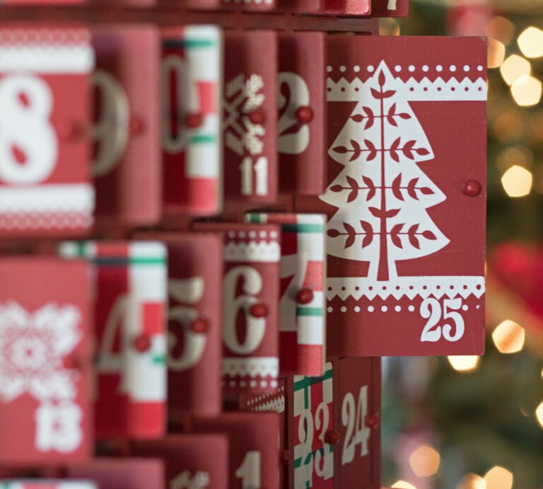 Roter Adventskalender mit weißen Zahlen und Weihnachtsbaum-Motiv auf Tür 25, weitere Türen teilweise geöffnet. | © Adobe Stock/ Janice
