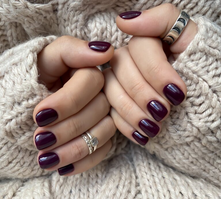 Zwei gepflegte Hände mit dunkelviolett lackierten Nägeln halten sich warm im Ärmel eines beigen Strickpullovers. | © Adobe Stock/ Наталья Плеханова