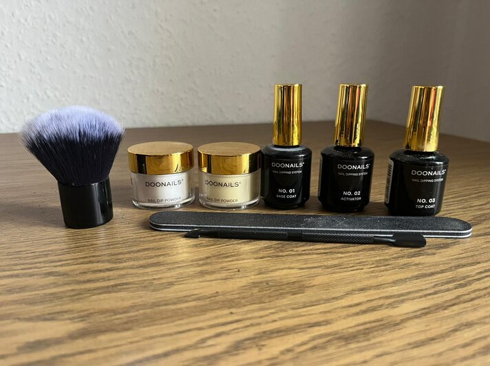 Komplettes Nagelset mit Dipping Puder, schwarzem Pinsel, Feile und drei gold-schwarzen Fläschchen ordentlich angeordnet. | © BILD der FRAU/ Kaja Wundersitz