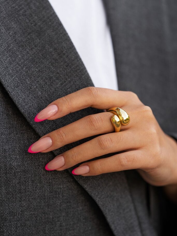 Eine Hand mit glänzendem, rosafarbenem Nagellack hält ein rosa Notizbuch, während die andere Hand sanft darüber ruht, vor einem lila Punktmuster. | © FreePik