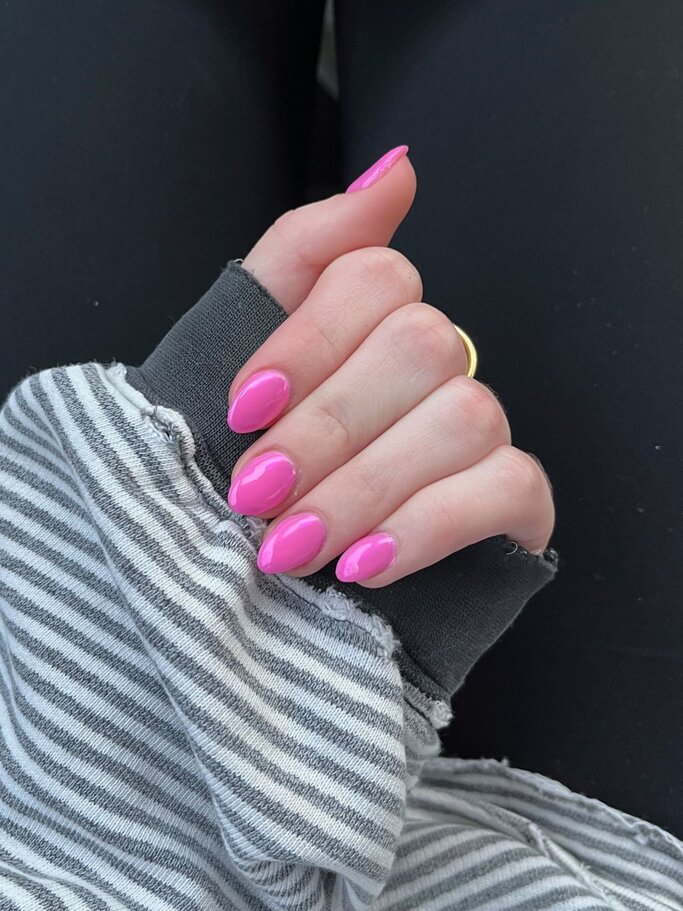 Eine Hand mit leuchtend pinken, glänzenden Nägeln trägt einen goldenen Ring und steckt in einem grau-gestreiften, lockeren Pulloverärmel. | © Adobe Stock/ Meghan