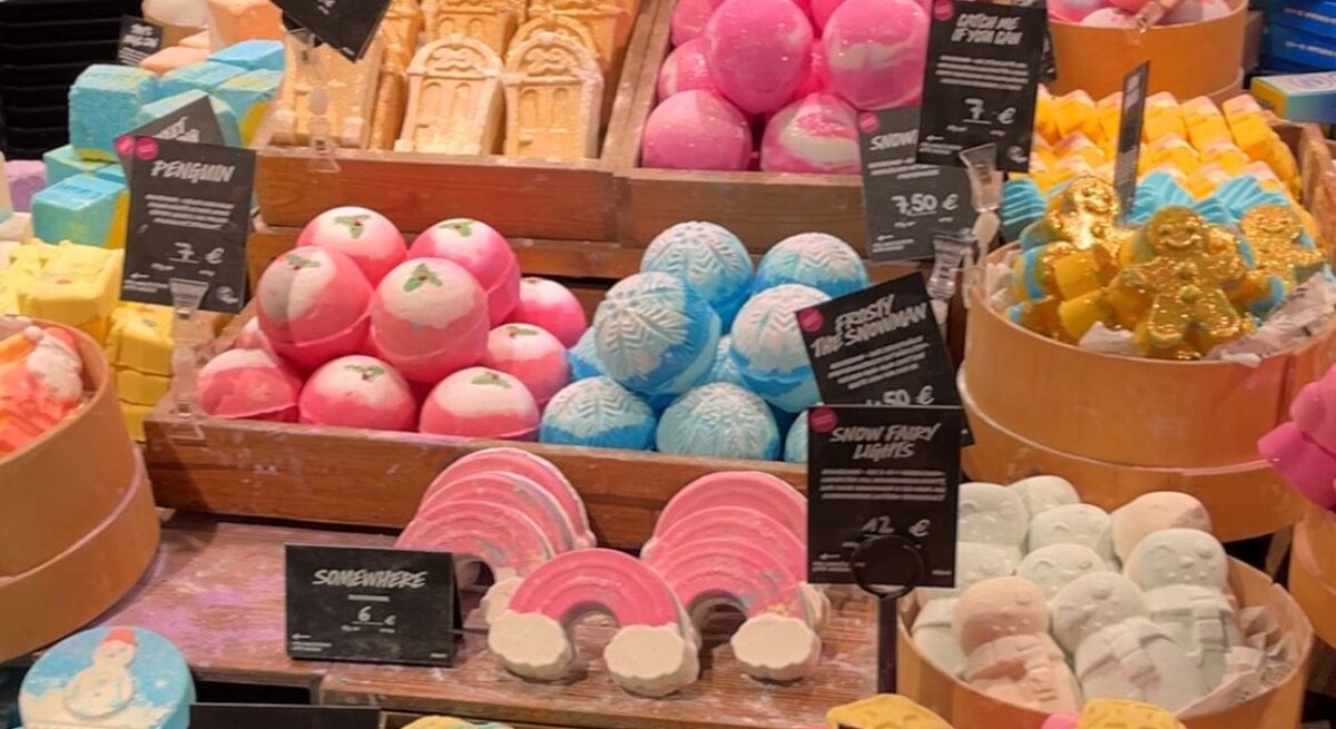 Farbige Badebomben und Seifen in verschiedenen Formen wie Regenbogen, Schneemänner und Lebkuchenmänner, dekorativ auf Holzkisten präsentiert.