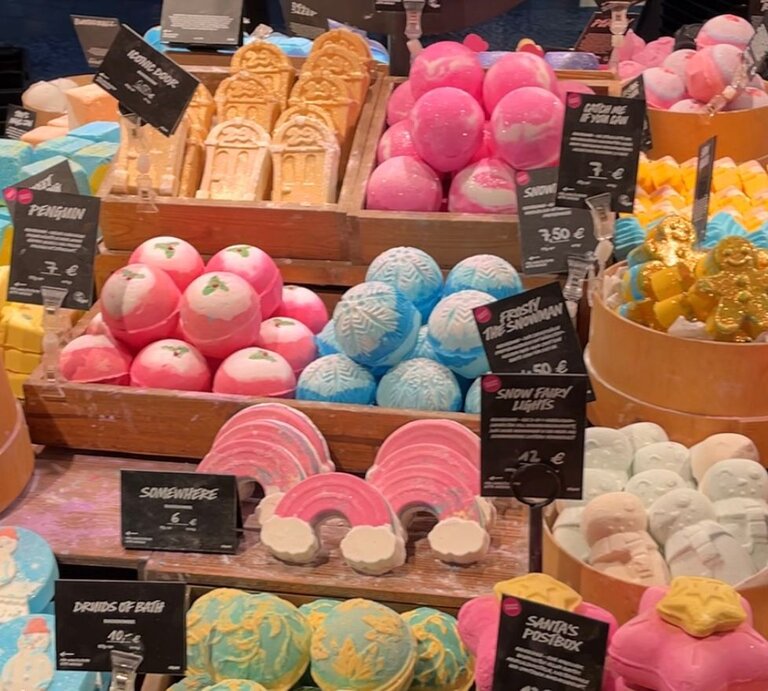 Farbige Badebomben und Seifen in verschiedenen Formen wie Regenbogen, Schneemänner und Lebkuchenmänner, dekorativ auf Holzkisten präsentiert. | © Kaja Wundersitz/ BILD der FRAU