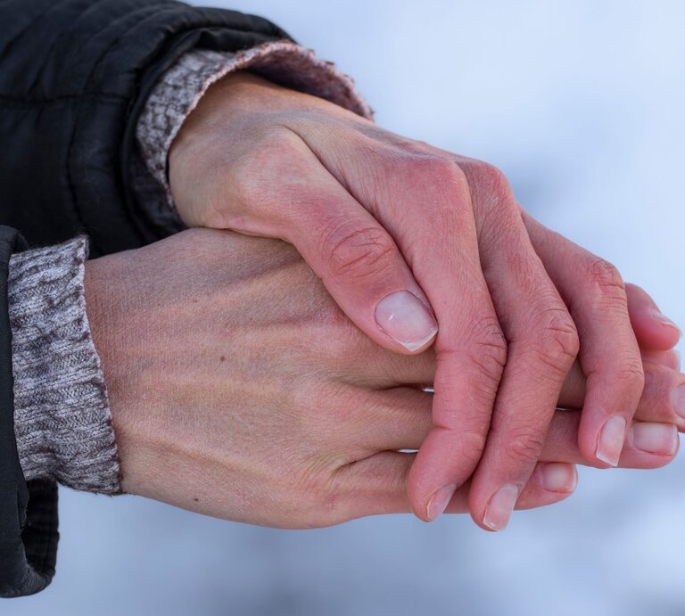 Hände, die ineinander gelegt sind, vermutlich um sich zu wärmen. Die Haut der Hände wirkt trocken und leicht gerötet, was auf kaltes Wetter oder trockene Winterluft hindeutet. | © Adobe Stock / Yuliya
