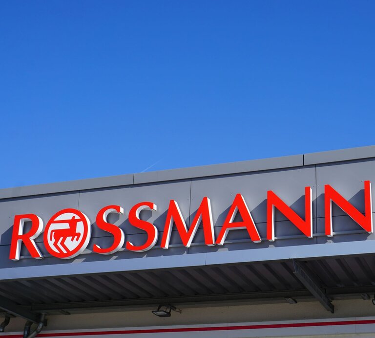 Rotes Rossmann-Logo auf grauer Fassade eines Geschäftes vor klarem, blauem Himmel. | © Adobe Stock/ Janet Worg