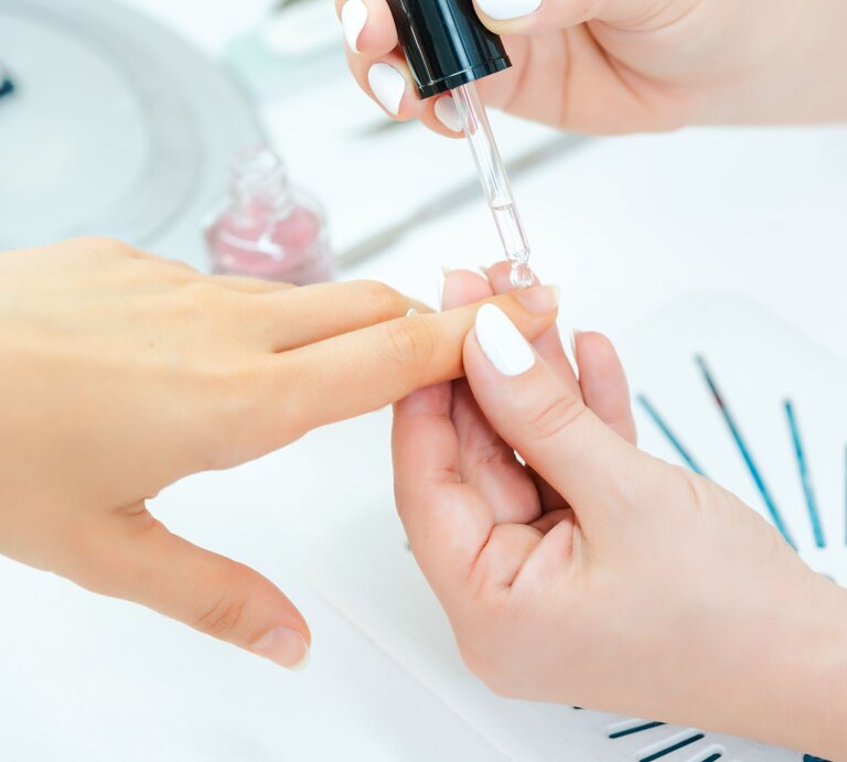 Nahaufnahme einer klassischen Maniküre: Nagelöl wird präzise mit einer Tropfpipette auf den Nagel einer Hand aufgetragen. | © Adobe Stock/ Kzenon
