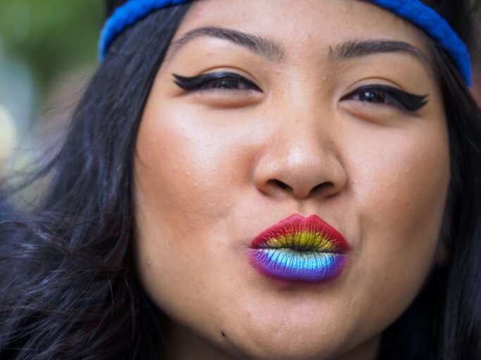 Nahaufnahme einer Frau mit blauer Mütze, buntem Regenbogen-Lippenstift und dramatischem schwarzen Eyeliner. | © Getty Images/ Merrill Images