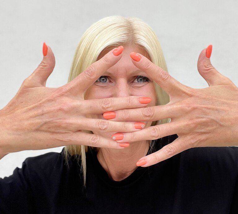 Topage-Model Renate Zott mit pfirsichfarbenen Fingernägeln – ihre Hände hält sie gekreuzt vor dem Gesicht. | © Renate Zott