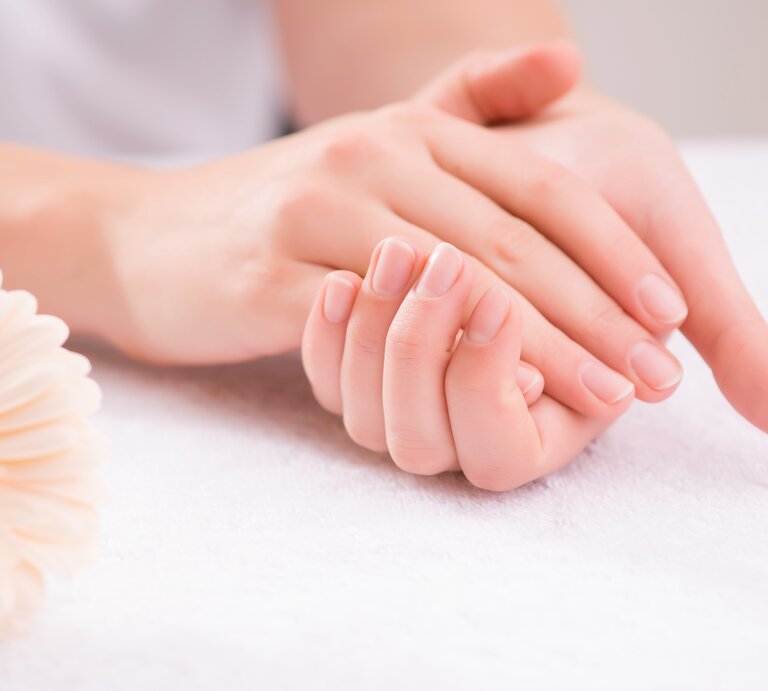 Gepflegte Hände mit sorgfältig manikürten Nägeln in einem dezenten Nude-Ton. Die Nägel sind kurz gehalten und haben eine natürliche, ovale Form. Eine Blume liegt neben den Händen. | © Adobe Stock / Viacheslav Yakobchuk