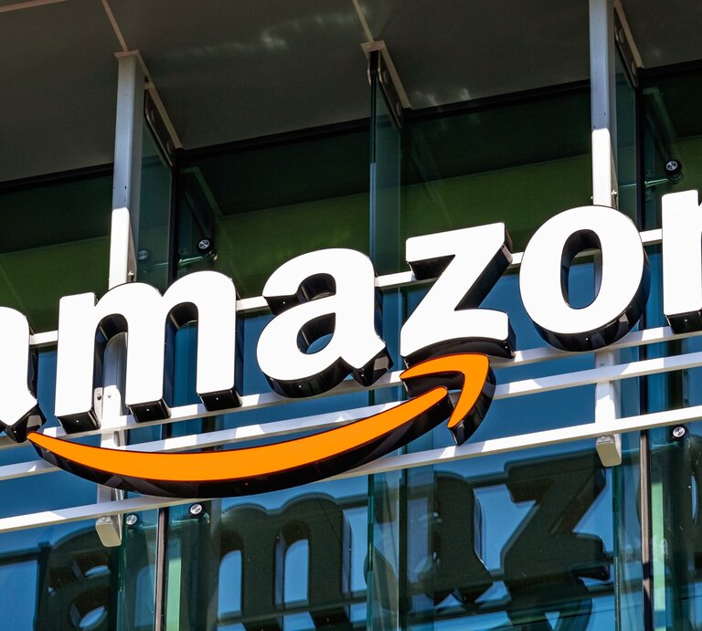 Nahaufnahme des bekannten Amazon-Schriftzugs mit orangem Pfeil auf Gebäudefront. | © AdobeStock/Sundry Photography