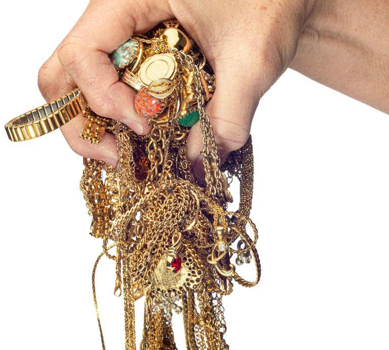 Hand, die einen Haufen von verknoteten Goldketten, Armbändern und anderen Schmuckstücken hält. Die Schmuckstücke sind stark ineinander verwickelt. | © Adobe Stock / Carolyn Franks
