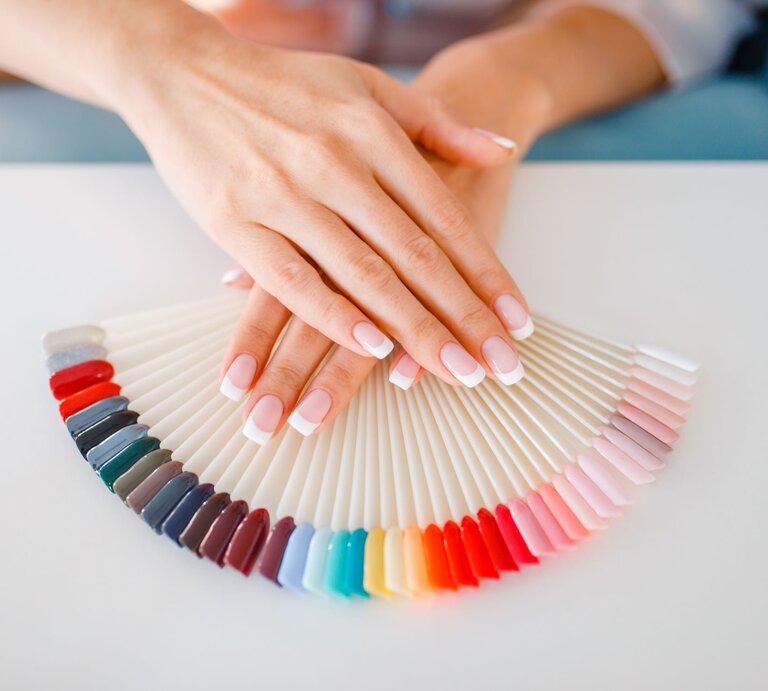 Nahaufnahme von Händen mit dezentem French Maniküre-Look, die einen Nagellack-Farbfächer präsentieren. | © Nomad_Soul