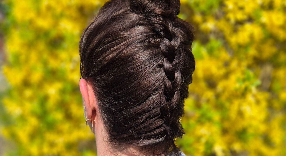 Zu sehen ist eine Frau, die die beschriebene Frisur trägt, mit braunen Haaren, vor einem Osterbusch