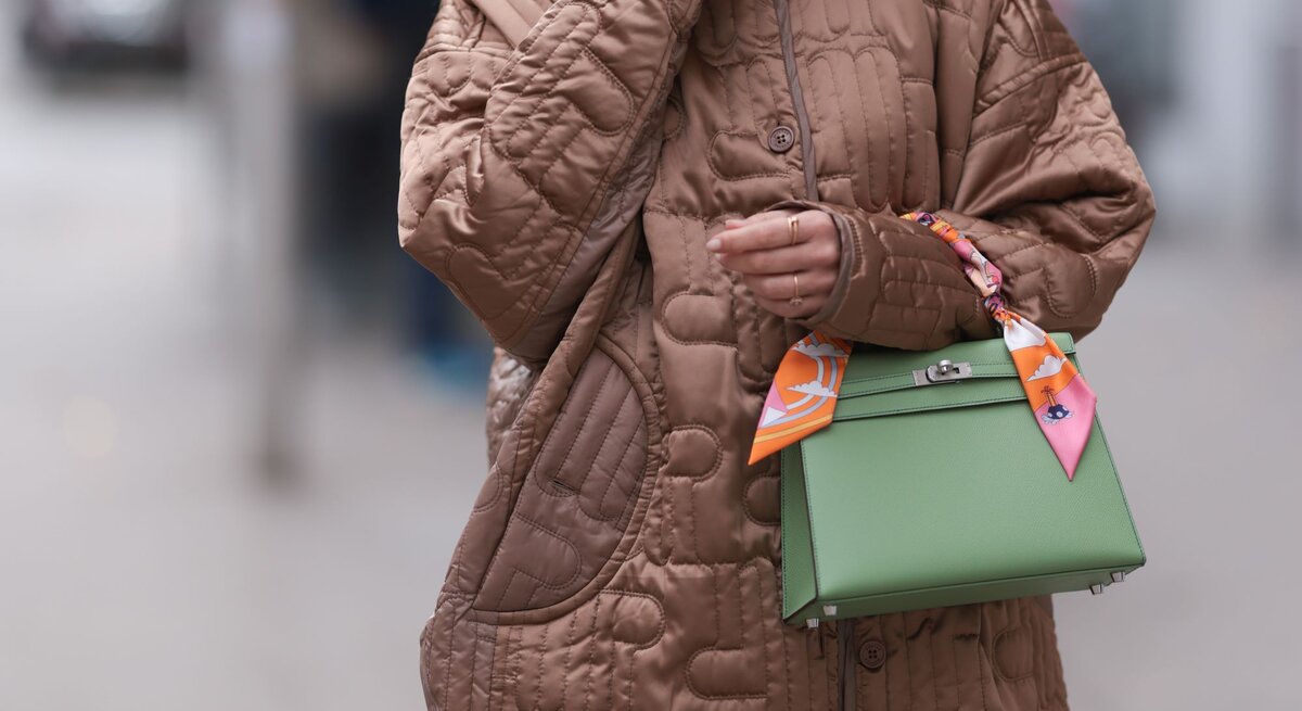 Zu sehen ist eine braune dünne Steppjacke mit einer grünen Handtasche