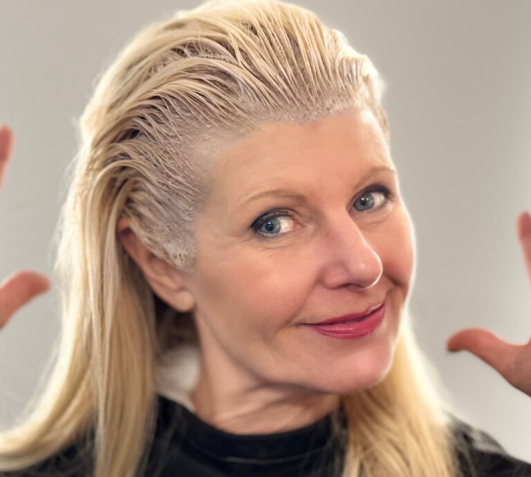Renate Zott beim graue Haare färben, lächelt in die Kamera und hebt fröhlich die Hände. | © Renate Zott