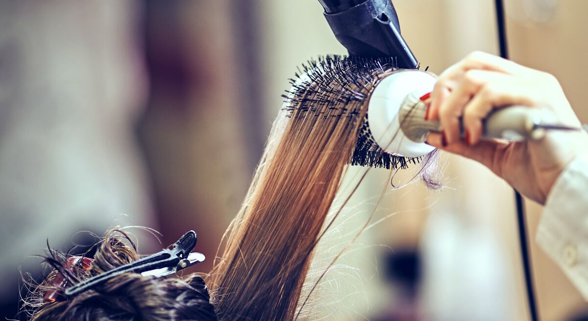 Zu sehen sind Haare, die mithilfe einer Rundbürste in ein Blowout geföhnt werden.