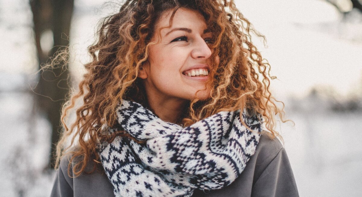 Zu sehen ist eine Frau mittleren Alters, die ihre Locken im Winter offen trägt