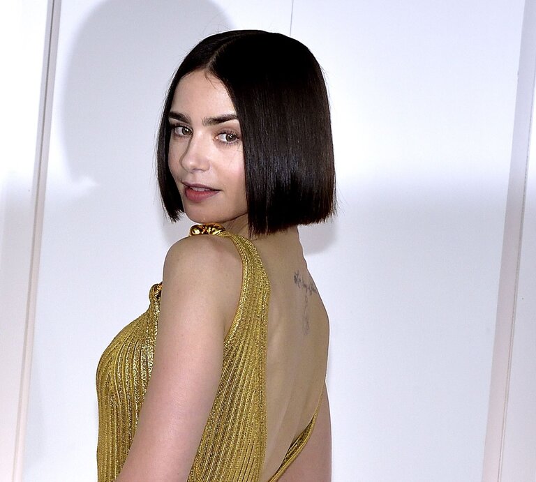 Frau mit einem bob-geschnittenen, dunklen Haar, die eine elegante, goldene Robe trägt. Sie steht mit dem Rücken zur Kamera und dreht sich über die Schulter, wobei sie direkt in die Kamera blickt. | © Getty Images / Mondadori Portfolio