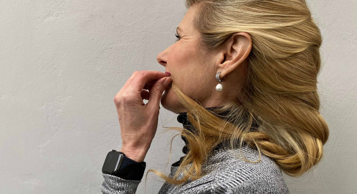 Frau mit blondem Haar, die eine elegante, seitlich geschwungene Frisur trägt. Ihr Haar ist sanft nach hinten gelegt und leicht geflochten.