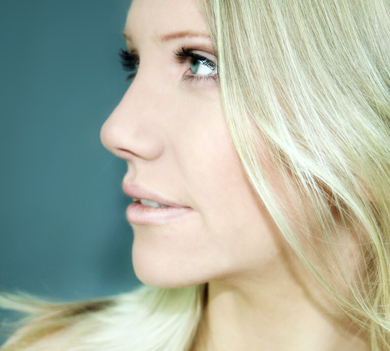 Frau im Profil mit langen, blonden Haaren, die einen Grünstich haben. Ihre Haare sind glatt und fallen sanft über ihre Schulter. Sie hat einen intensiven Blick | © Adobe Stock / Doreen Salcher