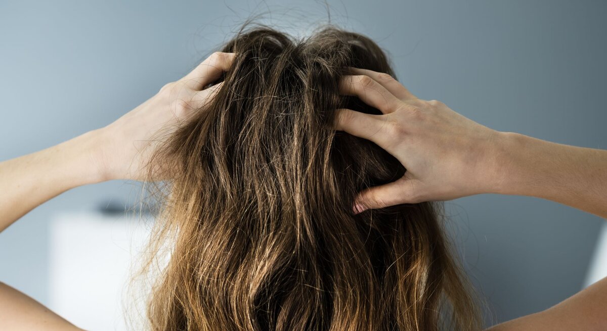 Frau von hinten mit verwuscheltem braunem Haar fasst sich mit den Händen in die Haare.