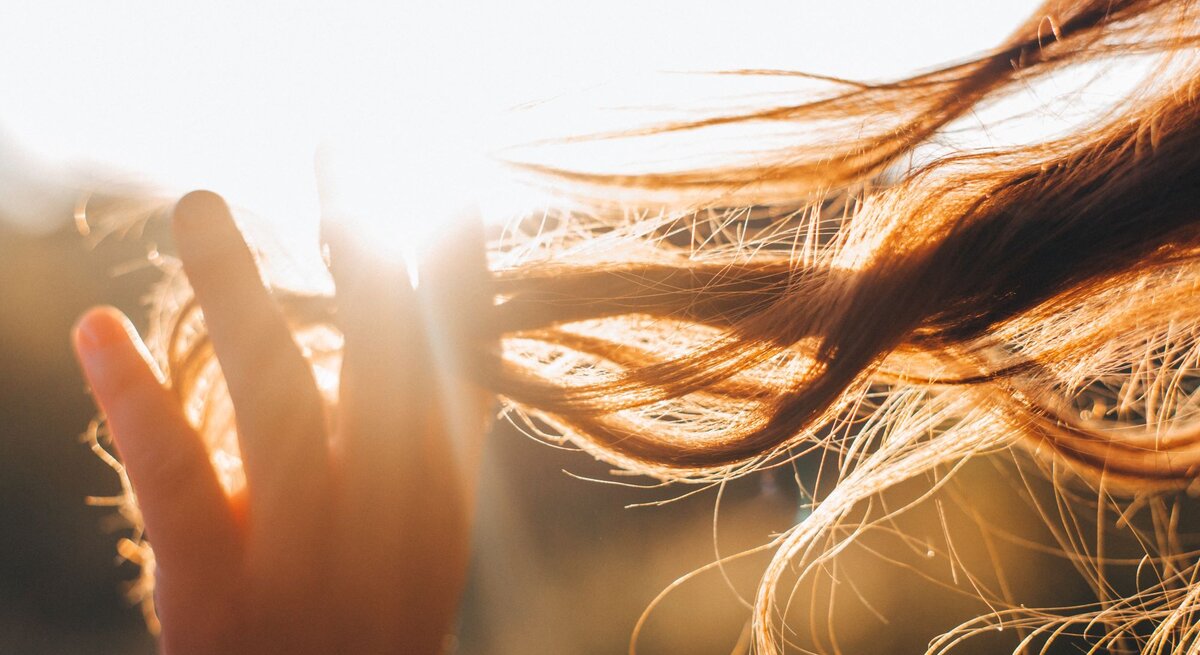 Nahaufnahme einer Hand, die durch langes Haar gleitet, das in der warmen Abendsonne leuchtet und sich im Wind bewegt.