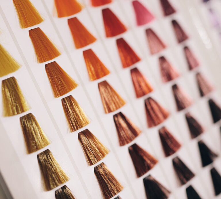 Fächer aus Haarfarbmustern in warmen Braun-, Kupfer- und Blondtönen auf weißem Karton, schräg fotografiert im Salonlicht. | © Adobe Stock/  Jacob Lund