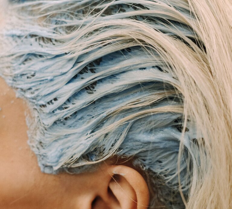 Detail einer Haarfärbung im Prozess. Die blonden Haare sind mit einer blauen Färbemasse bedeckt. Man kann die Struktur der Haare und die Cremigkeit der Farbe erkennen, die einen Kontrast zum natürlichen Blond der Haare bildet. | © Getty Images /	Nelson Martinez
