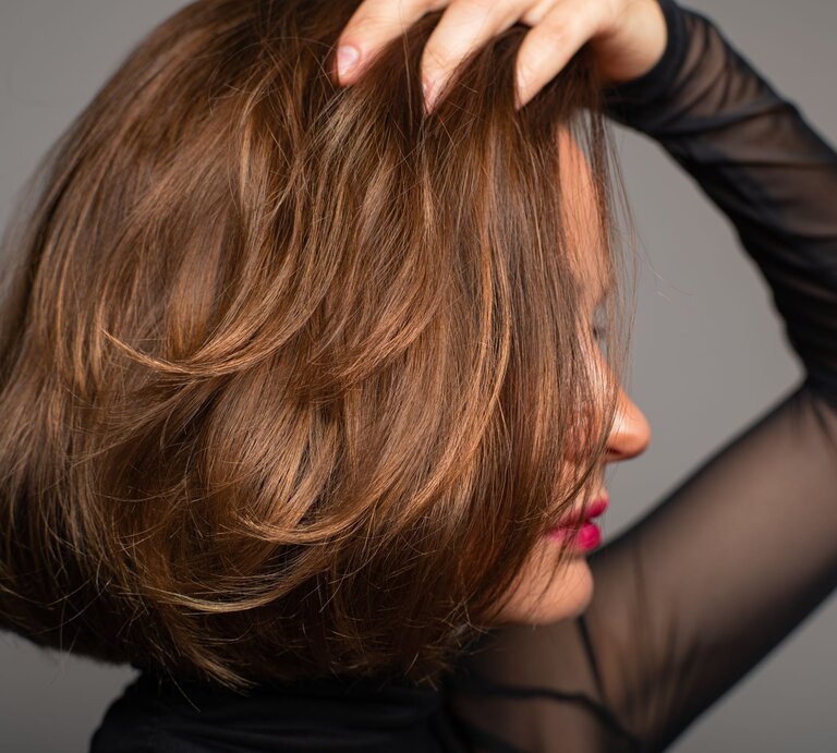 Frau, die mit ihrer Hand durch ihr kurz geschnittenes, voluminöses Haar fährt. Sie trägt einen dunklen, durchsichtigen Ärmel und hat leuchtend roten Lippenstift aufgetragen. Ihr Blick ist vom Betrachter abgewendet | © Adobe Stock / Dmytro Flisak