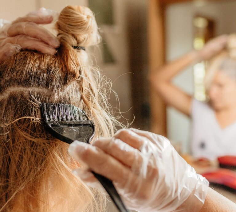 Frau färbt sich ihre Haare vor dem Spiegel mithilfe eines Pinsels, sie trägt Einmalhandschuhe | © Getty Images / Simon Skafar