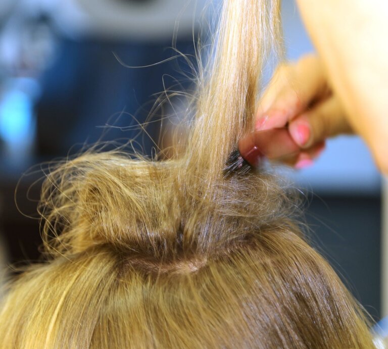 Eine Person toupiert den Haarwirbel auf dem Kopf einer Frau mit langem, blondem Haar, um Volumen zu erzeugen | © Adobe Stock / bildpunkte