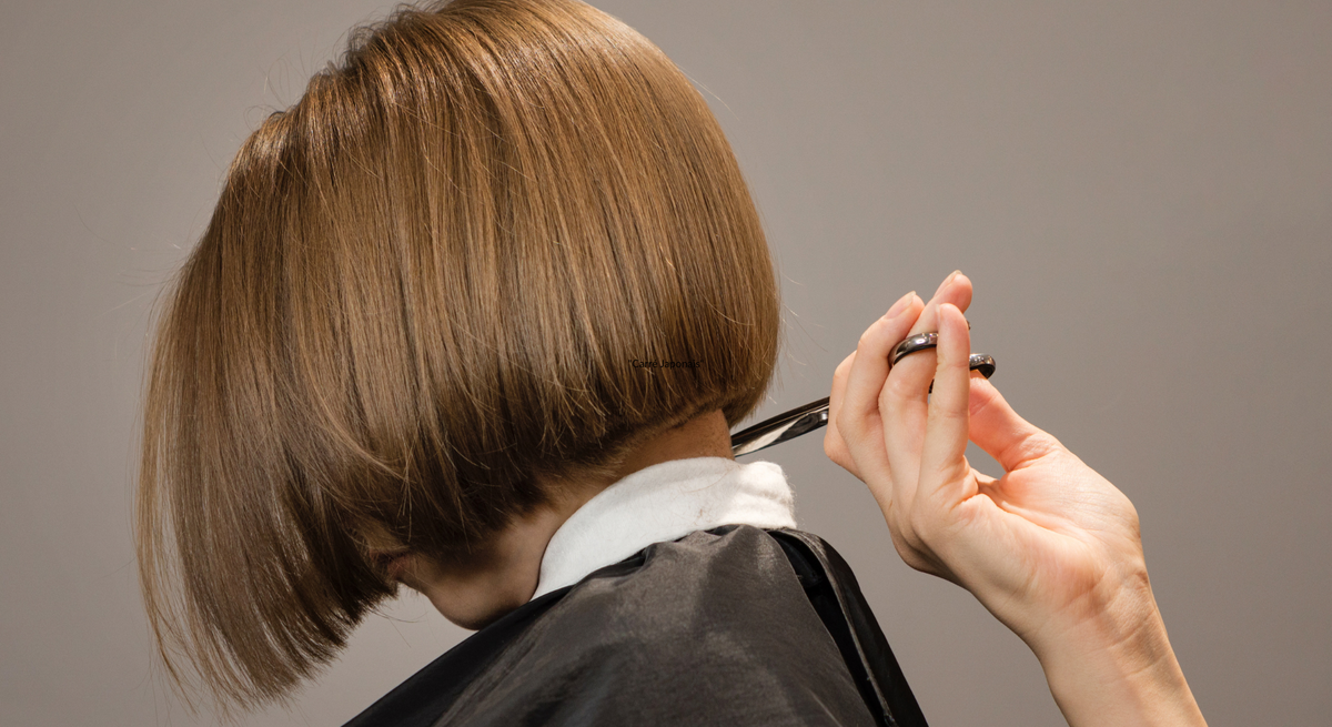 Ein Bob-Haarschnitt mit glänzendem, glattem, braunem Haar wird präzise von einer Hand mit Schere geschnitten.