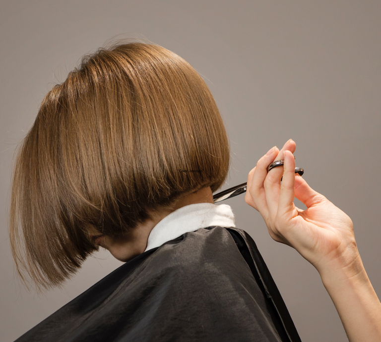 Ein Bob-Haarschnitt mit glänzendem, glattem, braunem Haar wird präzise von einer Hand mit Schere geschnitten. | © Canva