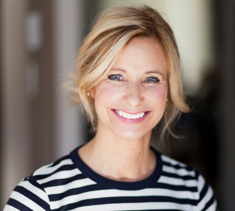 Frau mit blondem, leicht zerzaustem Haar trägt gestreiftes Shirt, aufgenommen in einem Innenraum mit verschwommenem Hintergrund. | © Canva