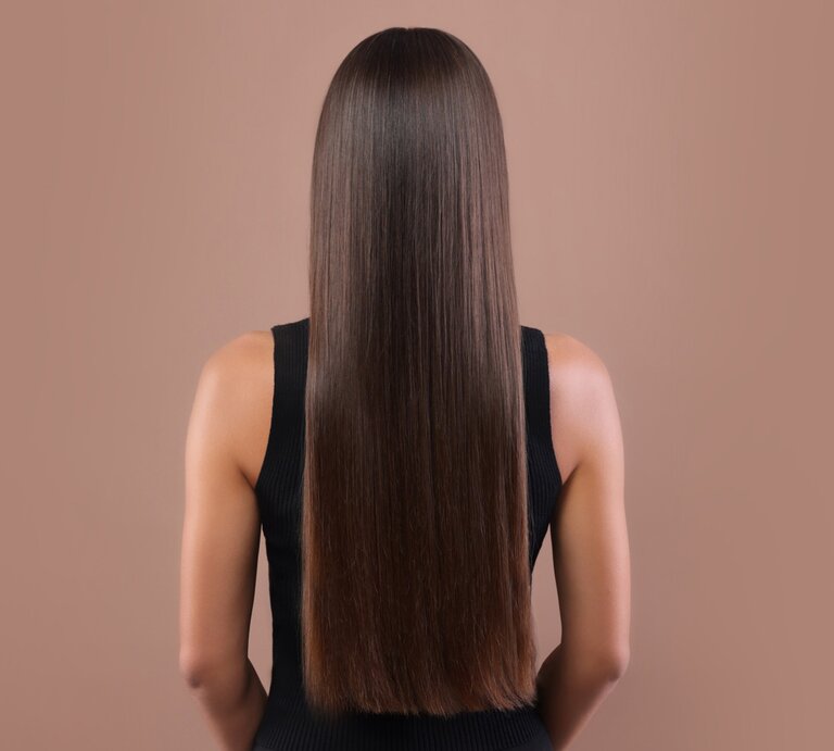 Zu sehen sind glänzende, glatte Haare vor einem beigen Hintegrund | © GettyImages/Liudmila Chernetska