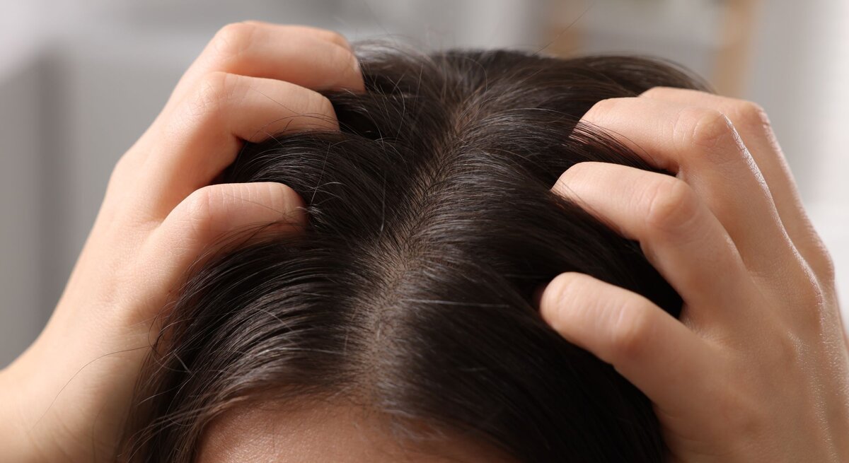 Eine Person mit dunklem Haar drückt ihre Fingerspitzen gegen die Kopfhaut, offenbar bei einer wohltuenden Kopfmassage.