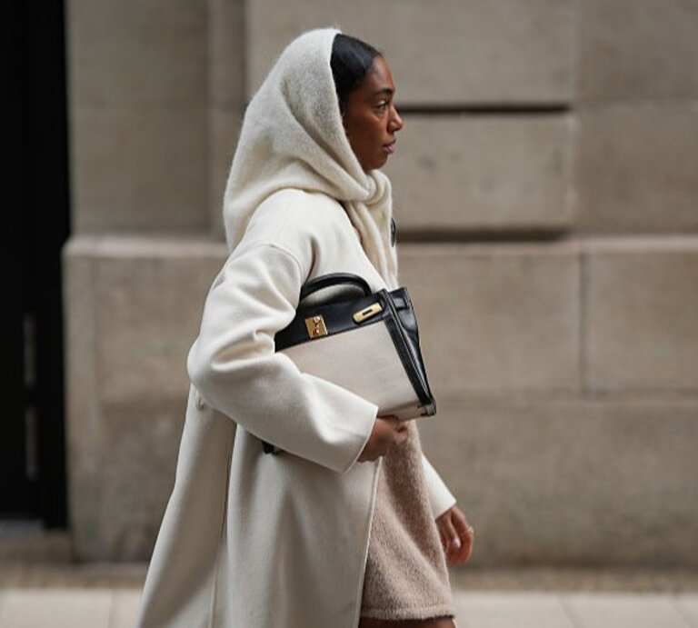 Zu sehen ist eine Frau, die ein beiges Wnteroutfit inklusive Schlupfschal trägt. | © GettyImages/Moritz Scholz