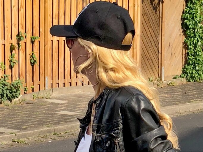 Seitenansicht einer Person mit lässigem Look aus Lederjacke, Cap und Sonnenbrille, umgeben von sommerlicher Szenerie an einem Holzzaun. | © Renate Zott