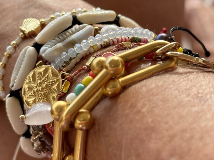Eine Auswahl von Armbändern mit goldenen Details, weißen Muscheln, bunten Perlen und feinen Anhängern schmückt ein Arm bei Tageslicht. | © Renate Zott