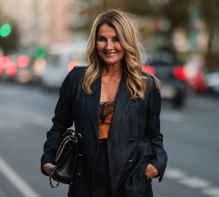 Frauke Ludowig  mit schwarzem Blazer und Handtasche lächelt selbstbewusst auf einer belebten Straße. | © Getty Images/ Jeremy Moeller / Kontributor