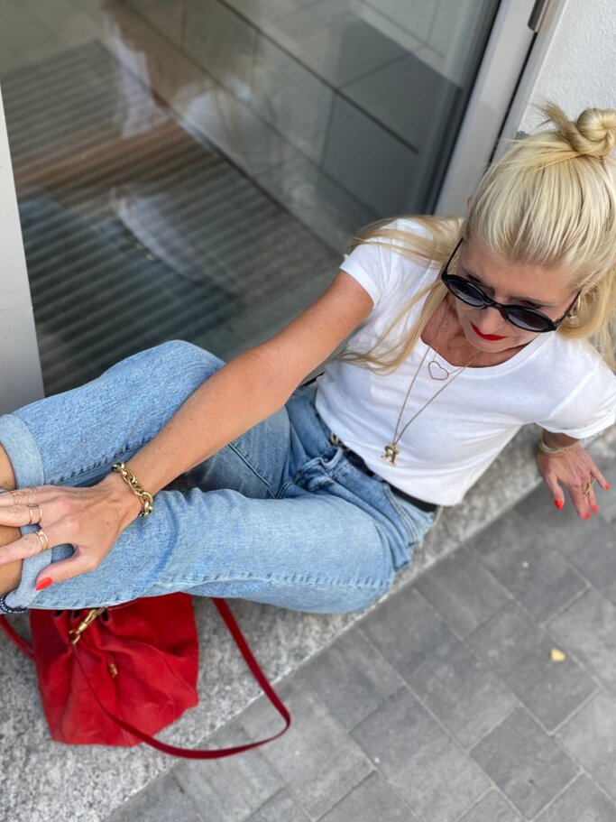 Blondierte Renate Zott mit Dutt posiert lässig auf einer Fensterbank, trägt rote Heels mit Nieten, Jeans und weißes T-Shirt. | © Renate Zott 