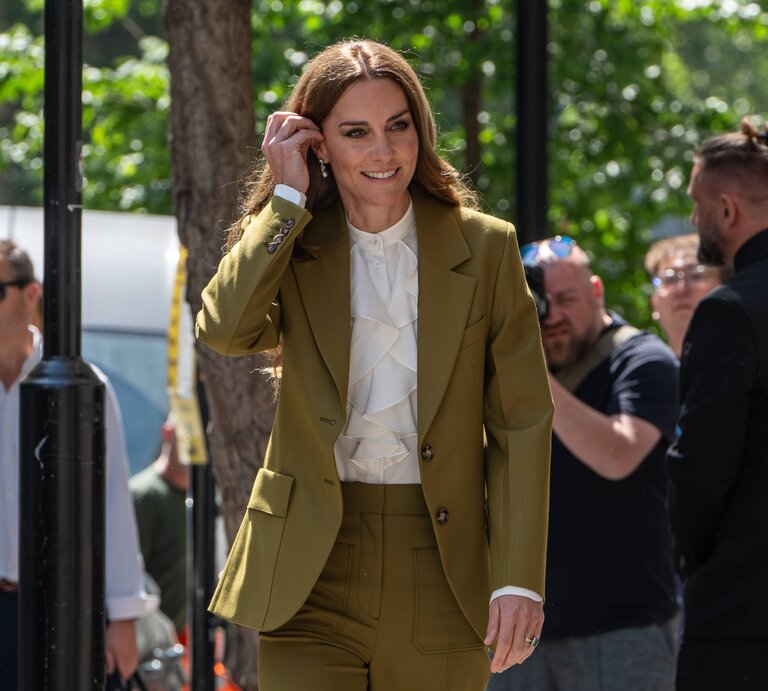 Prinzessin Kate  in olivgrünem Hosenanzug, Wedges Sandalen und weißer Rüschenbluse lächelt in die Kamera, umgeben von Fotografen und Passanten. | © IMAGO / ZUMA Press Wire