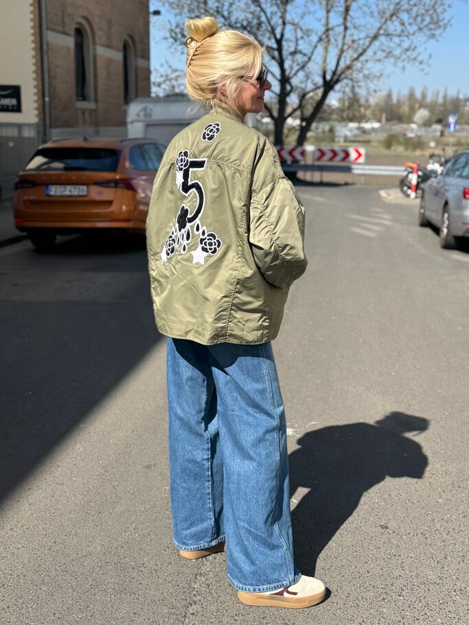 Renate Zott mit hochgesteckten Haaren in weiter Jeans und bestickter Jacke blickt entspannt auf leerer Straße. | © Renate Zott